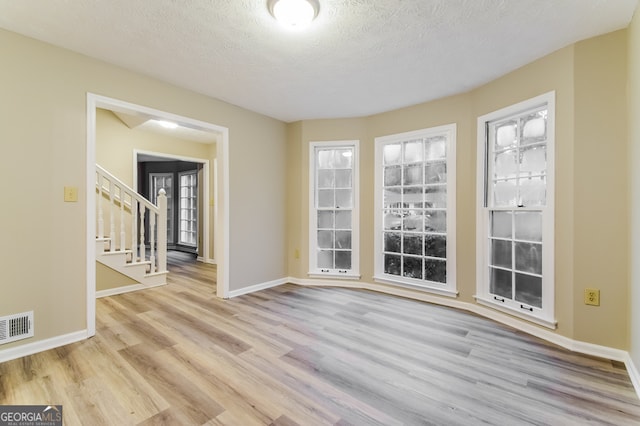 unfurnished room with light hardwood / wood-style flooring and a textured ceiling