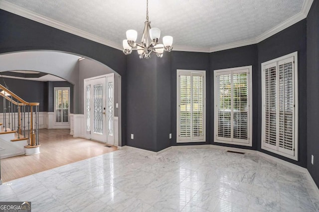 foyer featuring a chandelier, light wood-type flooring, a textured ceiling, and crown molding