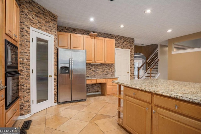 kitchen with black appliances, light stone counters, light brown cabinetry, a textured ceiling, and light tile patterned floors