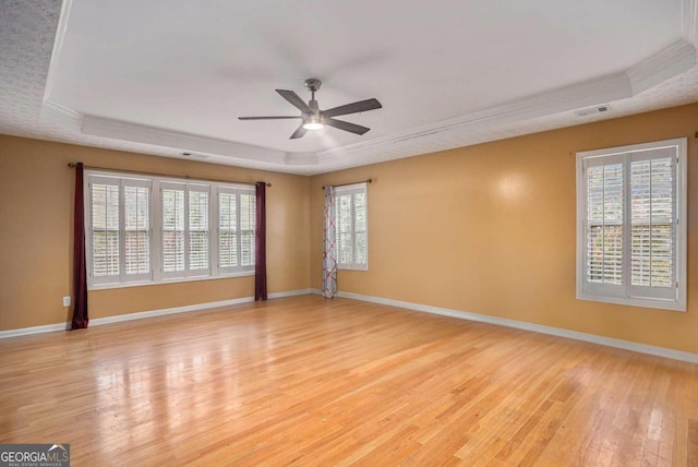 spare room with light hardwood / wood-style floors, ceiling fan, and a tray ceiling