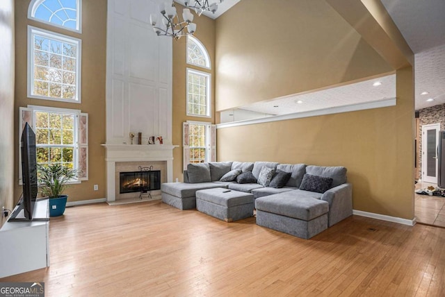 living room featuring a fireplace, light wood-type flooring, an inviting chandelier, and a towering ceiling