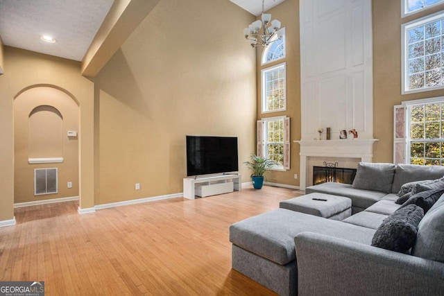 living room with a fireplace, a high ceiling, wood-type flooring, and an inviting chandelier