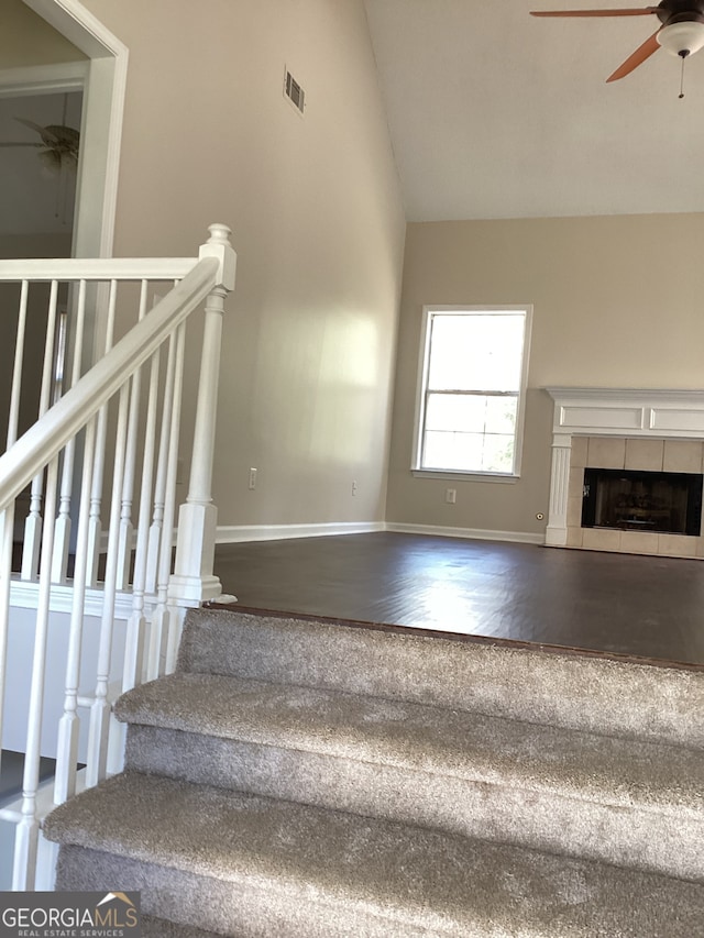 stairs featuring wood-type flooring, vaulted ceiling, ceiling fan, and a fireplace