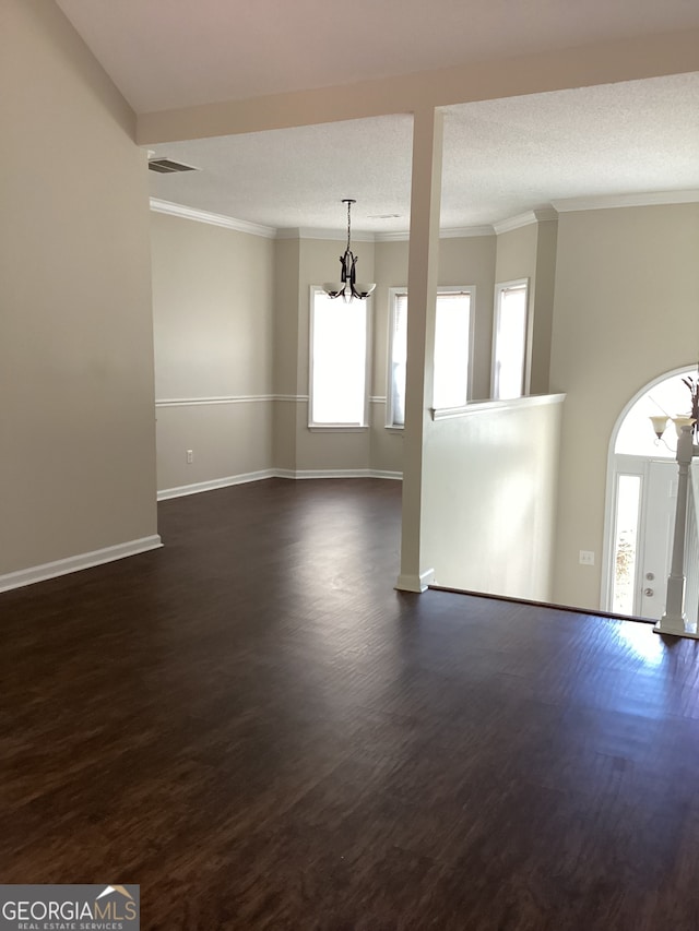 empty room with ornamental molding, a textured ceiling, dark hardwood / wood-style floors, and a chandelier