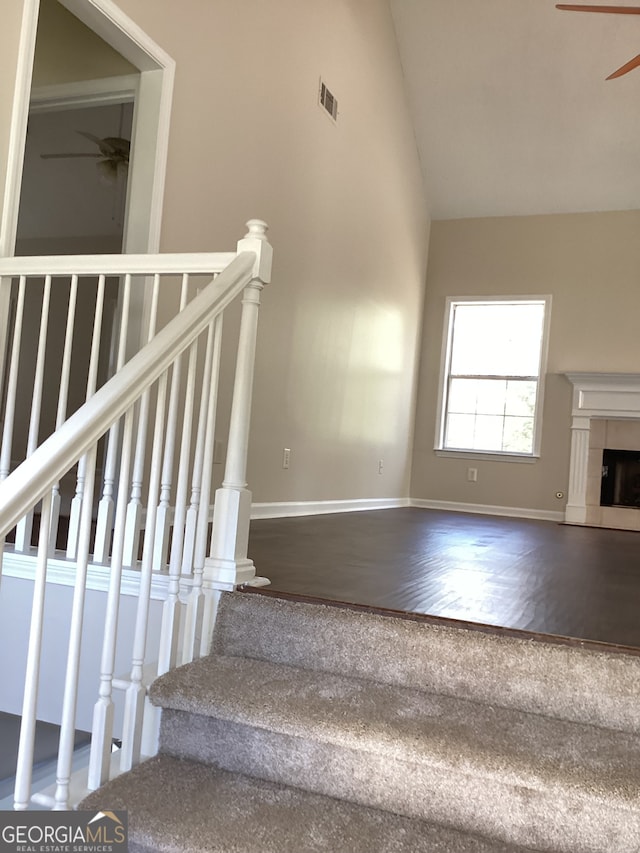 stairway with hardwood / wood-style floors, ceiling fan, a tile fireplace, and vaulted ceiling