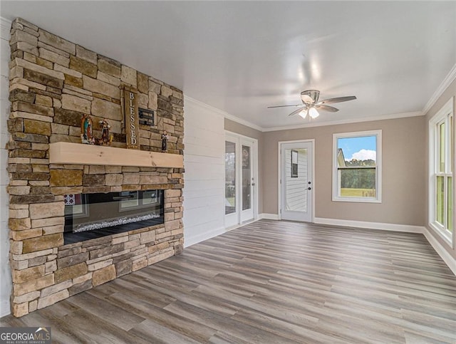 unfurnished living room with a stone fireplace, a wealth of natural light, hardwood / wood-style flooring, and crown molding