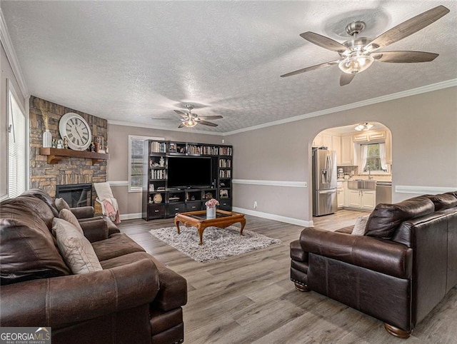 living room with ceiling fan, a textured ceiling, light wood-type flooring, and ornamental molding