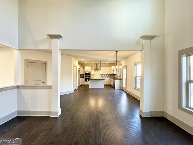 unfurnished living room featuring beamed ceiling, ceiling fan with notable chandelier, a wealth of natural light, and coffered ceiling