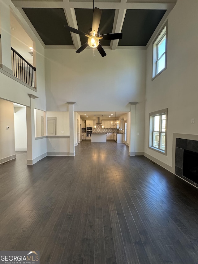 unfurnished living room with a tile fireplace, ceiling fan, dark wood-type flooring, coffered ceiling, and a towering ceiling