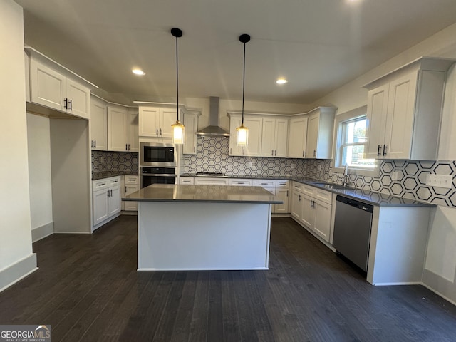 kitchen with a center island, wall chimney exhaust hood, decorative light fixtures, white cabinets, and appliances with stainless steel finishes