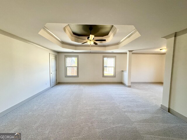 interior space with a tray ceiling, ceiling fan, light carpet, and ornamental molding