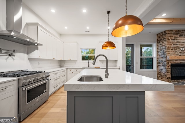 kitchen with a wealth of natural light, high end stainless steel range, wall chimney range hood, and an island with sink