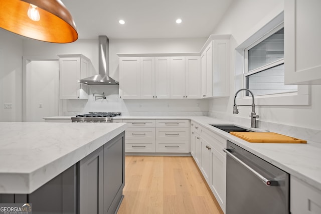 kitchen with stainless steel appliances, white cabinets, wall chimney exhaust hood, light stone countertops, and light hardwood / wood-style flooring