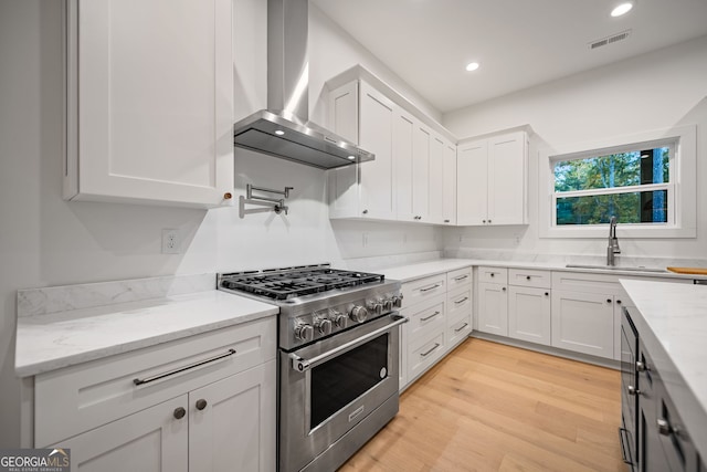 kitchen with sink, white cabinets, high end stainless steel range, light wood-type flooring, and wall chimney range hood