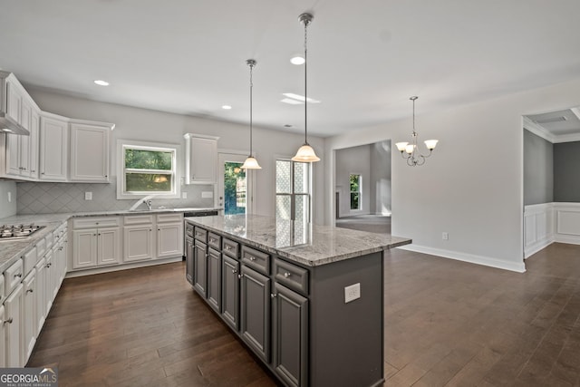 kitchen with light stone counters, a center island, white cabinets, and hanging light fixtures