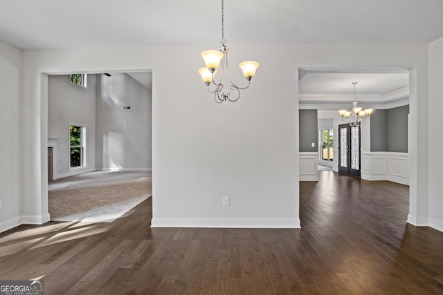 empty room with dark hardwood / wood-style flooring, a raised ceiling, and a notable chandelier