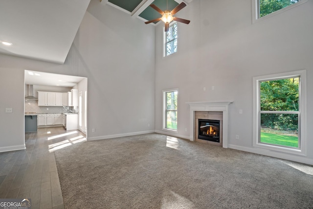 unfurnished living room with a tile fireplace, ceiling fan, and a high ceiling