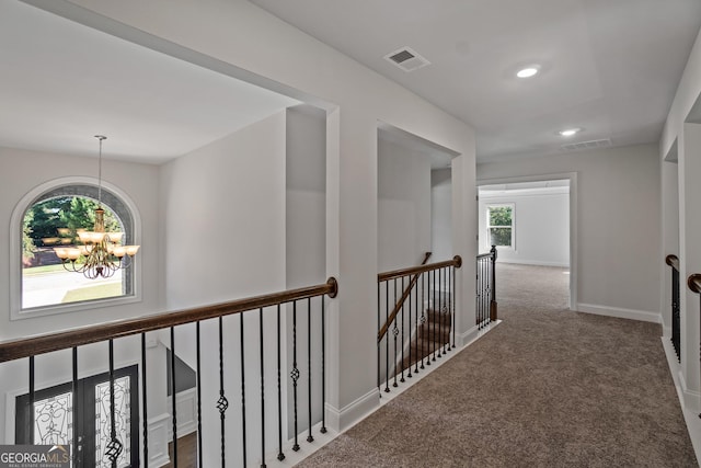 hall featuring dark carpet and a notable chandelier