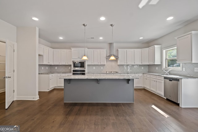 kitchen with white cabinets, a center island, wall chimney range hood, and appliances with stainless steel finishes