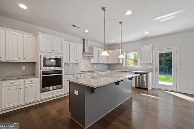 kitchen with wall chimney exhaust hood, a center island, white cabinets, and appliances with stainless steel finishes