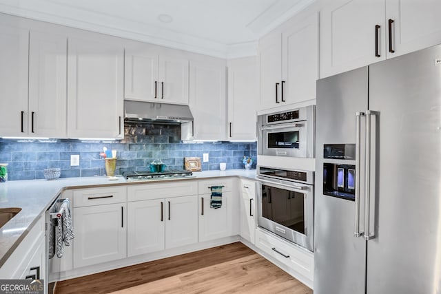 kitchen with light stone counters, appliances with stainless steel finishes, decorative backsplash, light hardwood / wood-style floors, and white cabinets