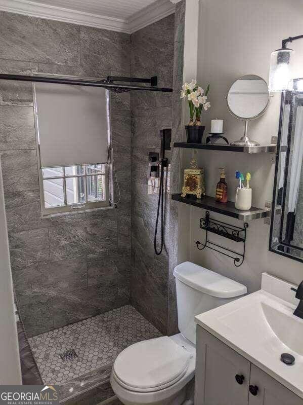 bathroom with vanity, toilet, a tile shower, and crown molding