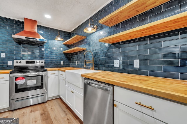 kitchen with wooden counters, wall chimney exhaust hood, stainless steel appliances, light hardwood / wood-style flooring, and white cabinets