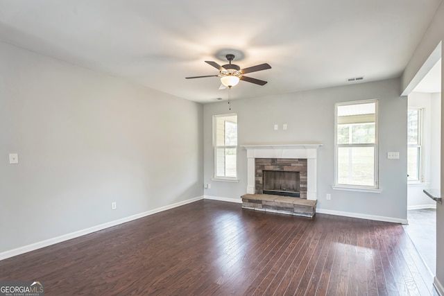 unfurnished living room with a stone fireplace, dark hardwood / wood-style flooring, and ceiling fan