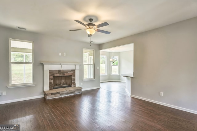 unfurnished living room featuring a stone fireplace, ceiling fan with notable chandelier, and dark hardwood / wood-style flooring