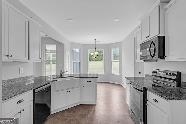 kitchen with white cabinets, stainless steel appliances, a notable chandelier, and dark stone countertops