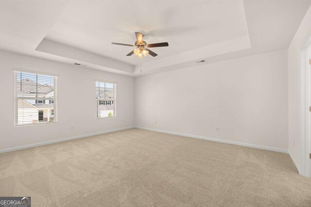 carpeted spare room featuring a tray ceiling and ceiling fan