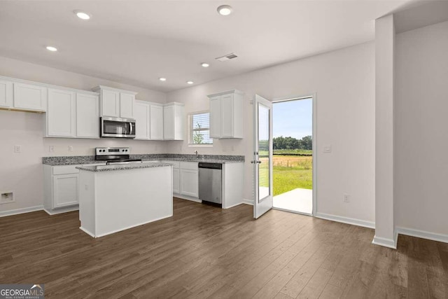 kitchen featuring white cabinetry, a center island, dark wood-type flooring, light stone countertops, and stainless steel appliances