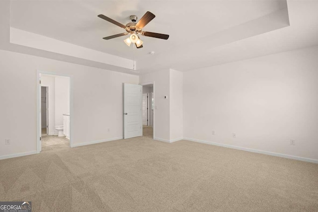 unfurnished bedroom featuring a tray ceiling, ensuite bath, ceiling fan, and light carpet