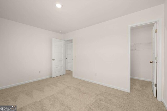 unfurnished bedroom featuring a spacious closet, a closet, and light carpet