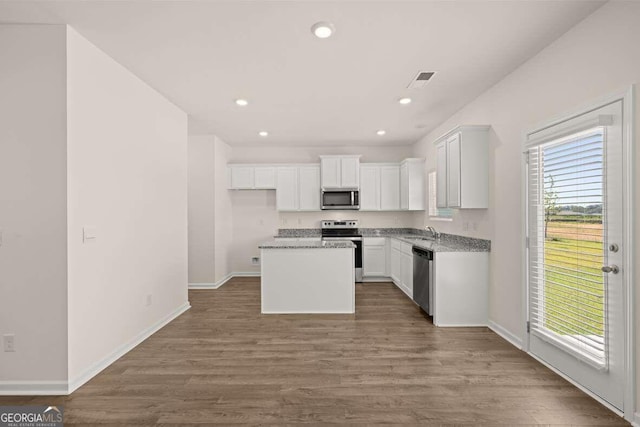 kitchen with white cabinetry, hardwood / wood-style floors, appliances with stainless steel finishes, a center island, and light stone countertops