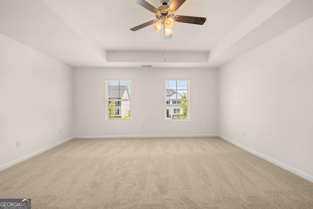 carpeted spare room with a tray ceiling and ceiling fan