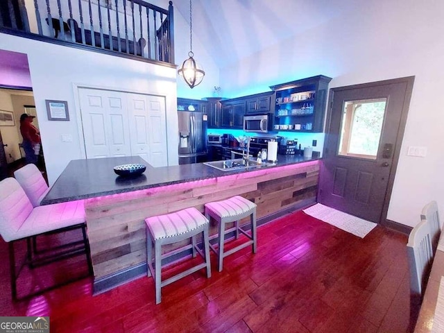 kitchen with kitchen peninsula, dark hardwood / wood-style floors, a breakfast bar, appliances with stainless steel finishes, and decorative light fixtures