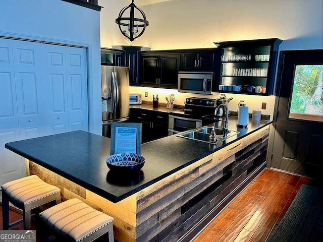 kitchen with appliances with stainless steel finishes, dark hardwood / wood-style flooring, sink, a breakfast bar, and a chandelier