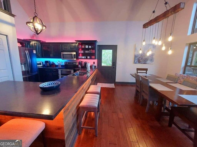 kitchen featuring stainless steel appliances, a kitchen bar, hanging light fixtures, a towering ceiling, and dark hardwood / wood-style flooring