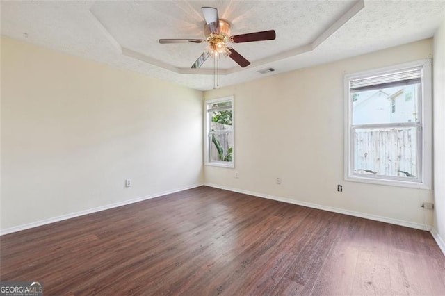 spare room with dark hardwood / wood-style flooring, a healthy amount of sunlight, ceiling fan, and a tray ceiling