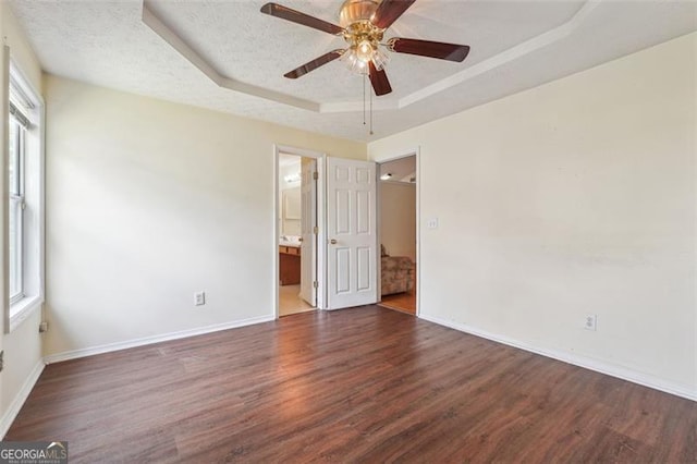 empty room with ceiling fan, dark hardwood / wood-style floors, a textured ceiling, and a tray ceiling