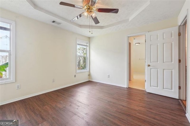 unfurnished bedroom with ensuite bathroom, dark hardwood / wood-style flooring, ceiling fan, and a raised ceiling