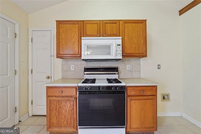 kitchen featuring backsplash, white appliances, vaulted ceiling, and light tile patterned floors