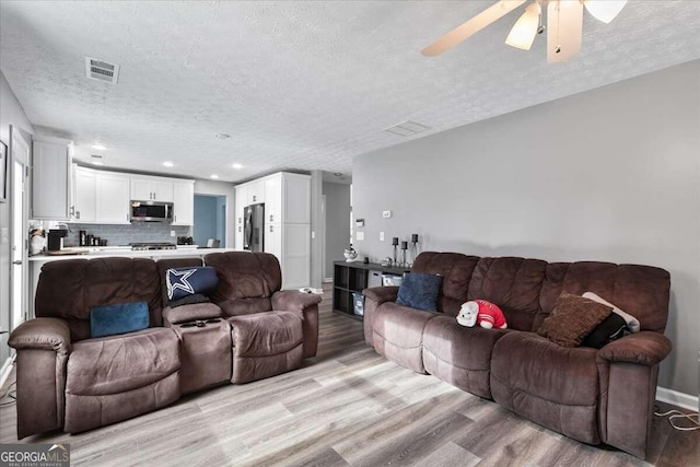 living room with light wood-type flooring, a textured ceiling, and ceiling fan