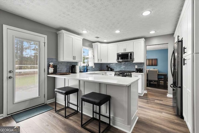 kitchen featuring white cabinetry, kitchen peninsula, appliances with stainless steel finishes, a breakfast bar area, and hardwood / wood-style floors