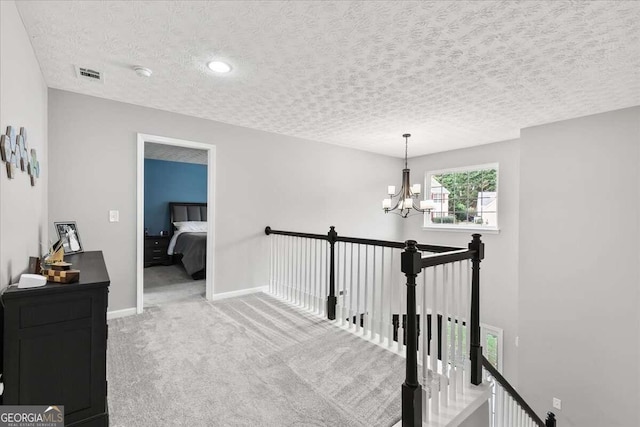 corridor with a textured ceiling, carpet floors, and a chandelier