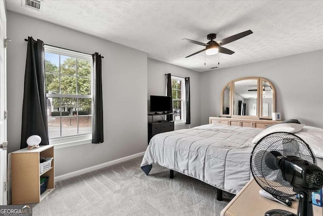 carpeted bedroom with a textured ceiling, multiple windows, and ceiling fan