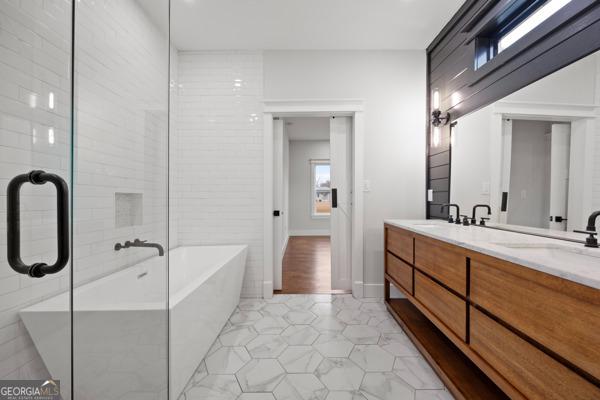 full bath with double vanity, a soaking tub, baseboards, and a sink