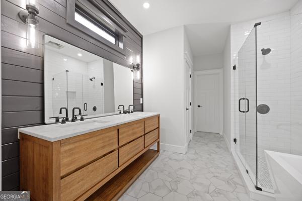 full bath featuring double vanity, marble finish floor, a freestanding tub, a shower stall, and a sink