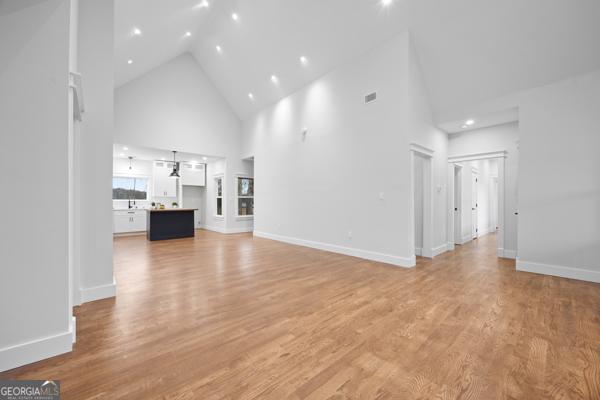 unfurnished living room featuring high vaulted ceiling, visible vents, light wood-style flooring, and baseboards